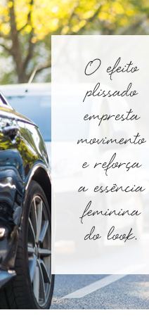 Modelo usando Saia Plissado andando na rua e com carro estacionado ao lado.