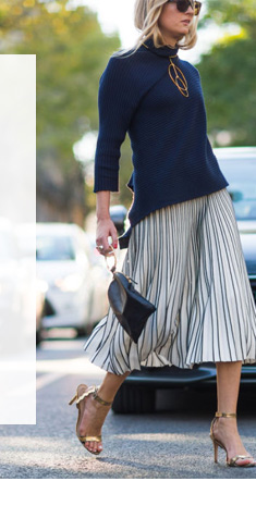 Modelo usando Saia Plissado andando na rua e com carro estacionado ao lado.